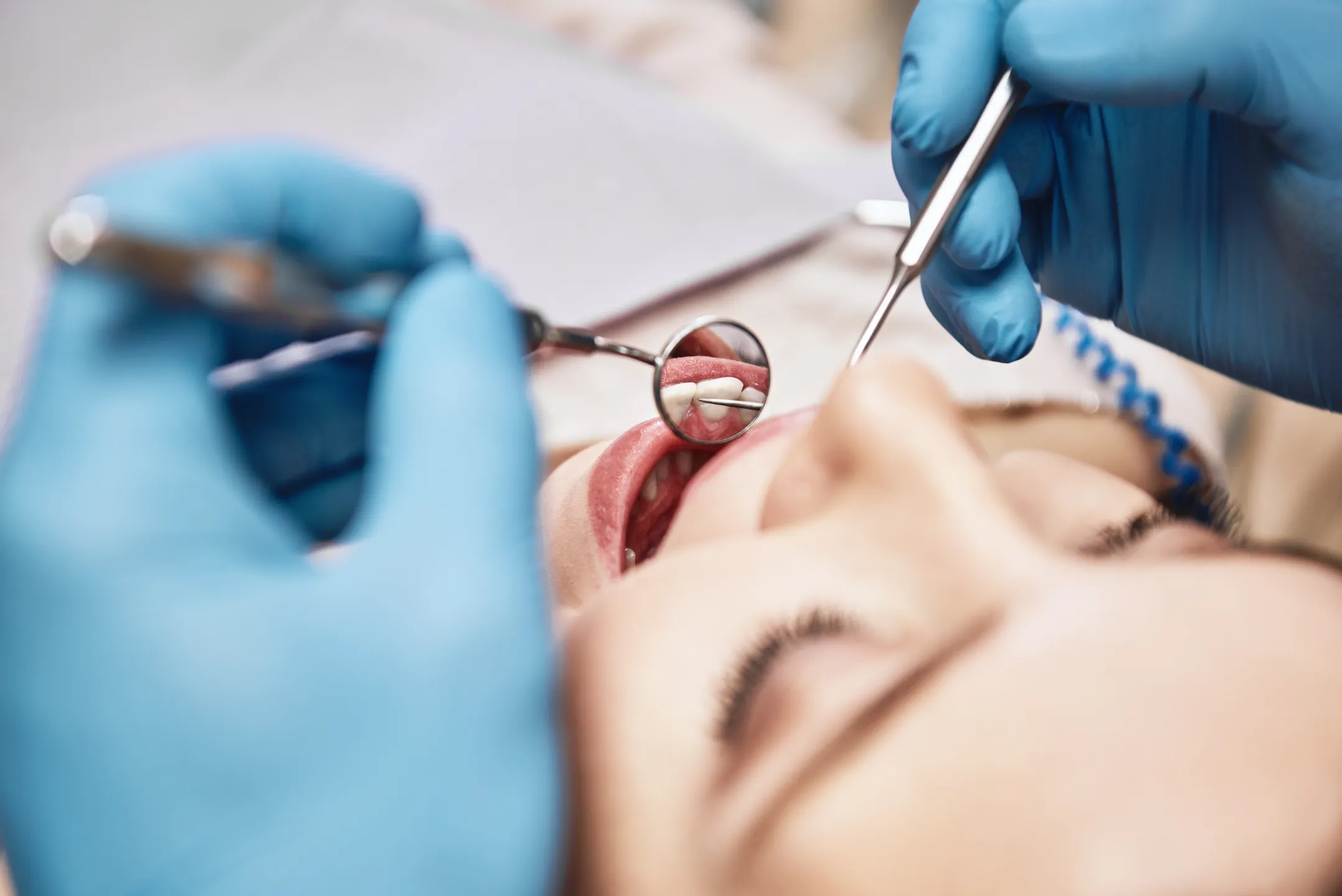 Dentist wearing blue gloves examining a patient’s teeth with dental mirror and probe.