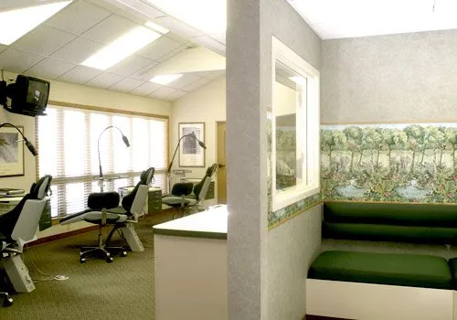 Waiting area with green bench and a room with salon chairs and mirrors separated by a partial wall.
