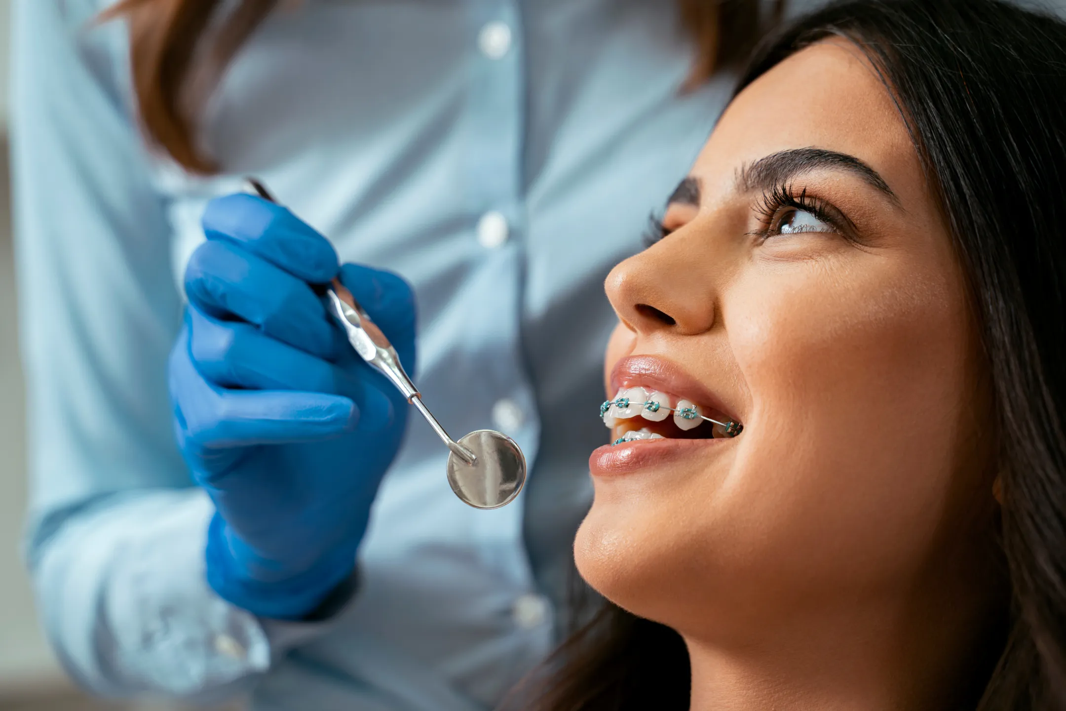 Close-up of smiling woman with braces undergoing dental checkup with a mirror tool.